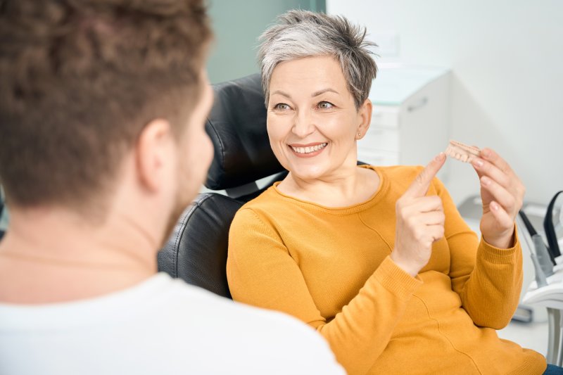 An older woman holding a jaw model while talking to her dentist