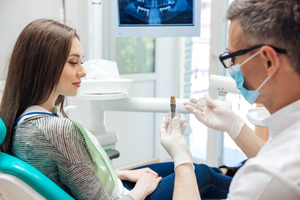 Dentist showing sample dental implant to woman with brown hair